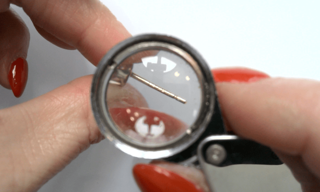 Using a jeweler's loupe to inspect a tiny gold mark on an earring post
