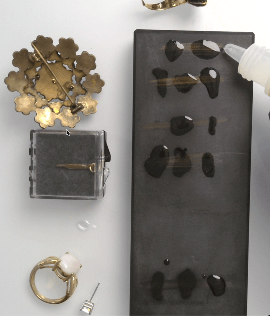 Separate drops of gold testing acid placed along metal streaks on a black touchstone